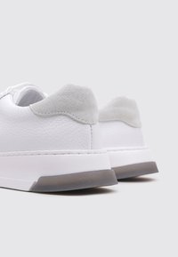 Zapatillas de piel blanca con acabado texturizado, acentos de piel de ante gris en el talón y una suela de goma blanca elegante con un reverso gris claro.