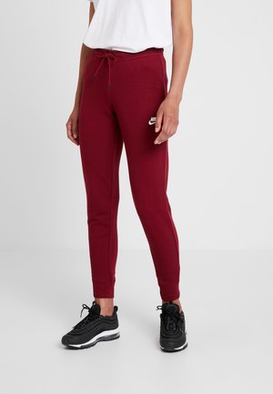 Person wearing burgundy Nike joggers with a drawstring waist, white cropped t-shirt, and black athletic sneakers on a plain background.