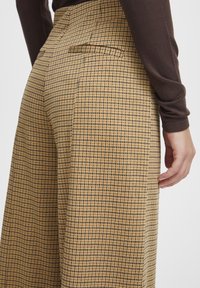 Bruna rutiga byxor med hög midja, vida ben och sidofickor. Tyget har ett rutigt mönster i beige och svart.