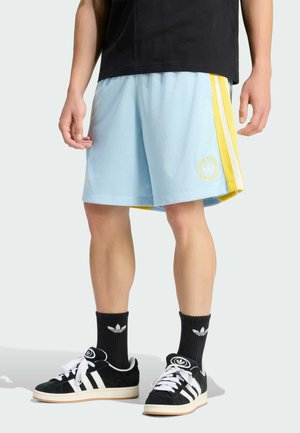 Pantalones cortos de malla azul claro con rayas laterales amarillas y un logo bordado. Combinados con zapatillas negras y calcetines negros acanalados.