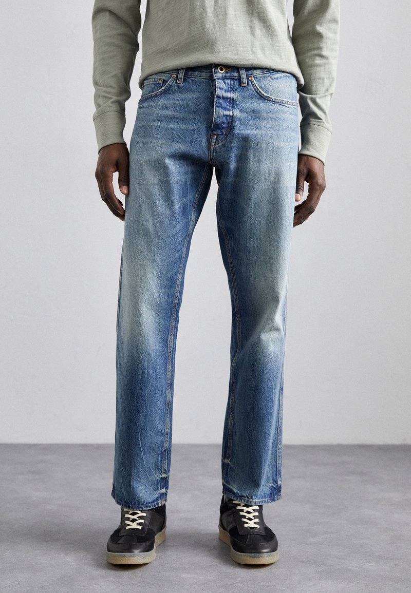 Ljusblå denimjeans med avslappnad passform, med urtvättade detaljer och fem fickor. Bärs med svarta sneakers och en olivgrön långärmad skjorta.