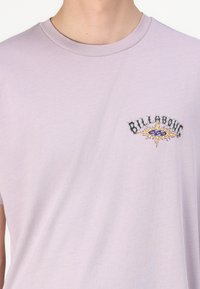 Lilakine medvilninė marškinėliai su apvaliu iškirpimu ir trumpomis rankovėmis. Yra juodas ir spalvingas išsiuvinėtas "Billabong" logotipas ant krūtinės.