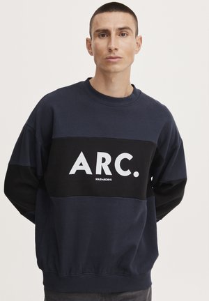 Navy blue sweatshirt with black accents, featuring a bold, white "ARC." logo and a relaxed fit. Soft, textured fabric, crew neck design.