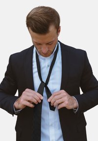 Mustade tekstuuridega lipsu seadmine mustas ülikonnas ja valges särgis, keskendudes lipsu keerukale mustrile ja kangastele. 