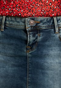 Gonna di denim blu medio con una leggera sfumatura, caratterizzata da un bottone metallico e cuciture gialle lungo le tasche e le cuciture.