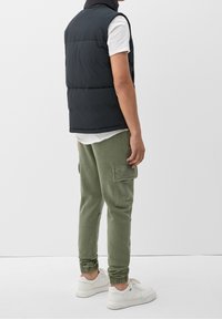 Schwarze Wattierweste mit hohem Kragen, kombiniert mit olivgrünen Cargo-Hosen und weißen Sneakers. Einfaches Design und weicher Stoff.
