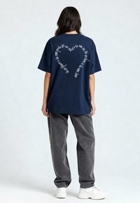 Jūros mėlynos spalvos per didelis marškinėlis su baltu tekstu širdies forma ant nugaros. Minkšta medvilnė, trumpomis rankovėmis ir laisva fit.