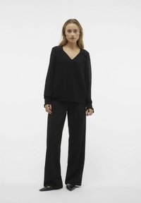 Blusa nera a maniche lunghe con scollatura a V e tessuto testurizzato. Indossata con pantaloni neri a gamba larga e ballerine nere con punta.