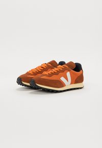 Brune semskede og mesh sneakers med oransje snøring og en hvit V-logo. Har teksturert overdel og sort gummisåle.