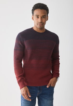 Röd och marinblå randig stickad tröja med rund halsringning och ribbade ärmavslut, tillsammans med blå jeans. Har strukturerat tyg och åtsittande design.