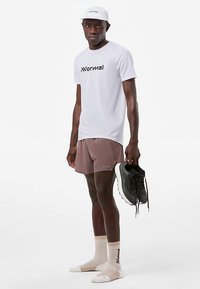 Hvit kortermet skjorte med sort logo, lysebrune shorts, beige sokker og svarte løpesko holdt i hånden mot en hvit bakgrunn.