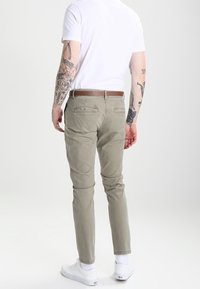 Chino en coton gris clair avec une coupe ajustée, présentant un devant plat et deux poches arrière. Porté avec un t-shirt blanc et des sneakers blanches.