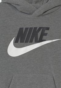 Grå huvtröja i bomullsblandning med en stor svart "NIKE"-logga och en vit swoosh-design på framsidan. Har en känguruficka.