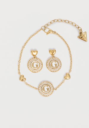 Gold-tone bracelet and earrings set with heart accents, crystal-studded circles, and letter "G" detailing, featuring a Guess logo charm.