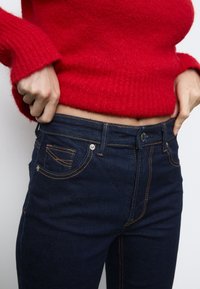 Temno modri jeans s pomarančnim šivanjem in obliko s petimi žepi, spono in tesnim prileganjem okoli pasu.