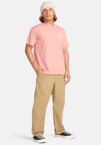 Light pink cotton t-shirt with a round neckline and short sleeves, paired with tan corduroy pants and black low-top sneakers.