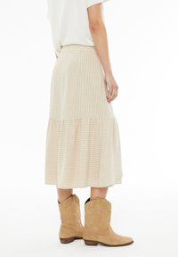 Falda midi beige con relieve y dobladillo en capas, que presenta rayas verticales. Combinada con botas de vaquero marrón claro. Textura suave, diseño casual.