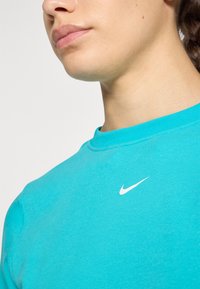 Türkises Nike-Sweatshirt mit Rundhalsausschnitt, weicher Textur, enganliegender Silhouette und weißem Nike-Logo auf der Brust.