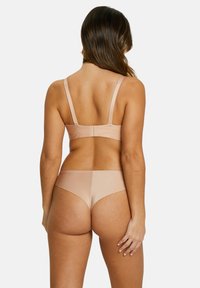Ensemble de soutien-gorge et culotte en nude, fabriqué dans un tissu lisse et extensible. Le soutien-gorge est doté de bretelles ajustables et d'une fermeture à crochets, avec des bords sans couture sur la culotte.