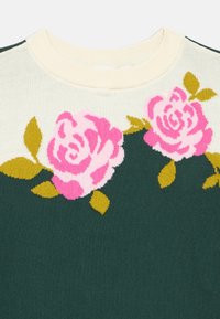 Kötött zöld pulóver nagy rózsaszín rózsákkal és zöld levelekkel. Krémszínű bordázott nyakrésszel. Lágy tapintású, virágmintás.