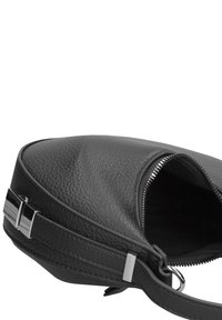 Zwarte leren tas met een textuur, ronde vorm, ritssluiting en metalen accenten aan de schouderband. Van binnen donker.