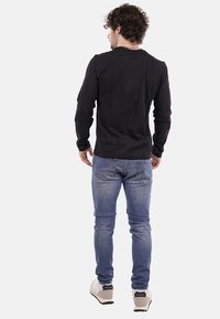 Maglietta nera a maniche lunghe in cotone, slim fit, abbinata a jeans in denim azzurri e sneakers grigie. Design semplice con colletto tondo.