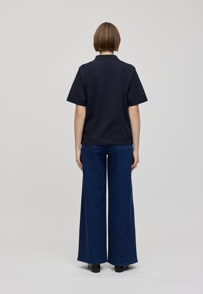 Jūras spēku polo krekls ar īsām piedurknēm, apvienots ar plašām zilo denimu džinsiem. Minimalistisks dizains, gluda tekstūra un vienkrāsaini toņi.