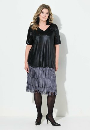 Zwarte, glanzende top met korte mouwen en een V-hals, gecombineerd met een grijze fringed rok. Model draagt zwarte hoge hakken en accessoires.