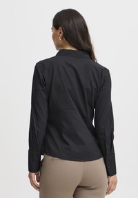 Camicia nera a maniche lunghe con design colletto, polsini abbottonati e tessuto liscio, con una vestibilità sartoriale per un aspetto raffinato.