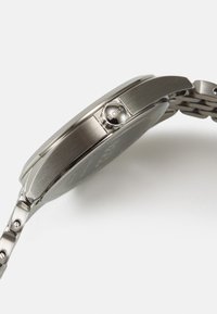 Montre en acier inoxydable avec une finition argentée polie, boîtier rond et design de bracelet. Présente une couronne proéminente avec le logo "BOSS".