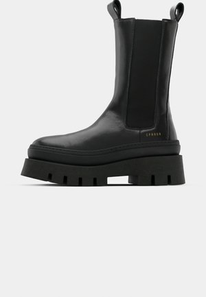 Black ankle boots with a smooth leather finish, elastic side panels, and a chunky, textured platform sole, featuring a logo detail.