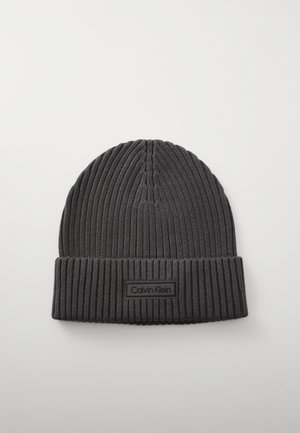 Beanie lavorato a maglia di colore grigio scuro. Presenta una texture a coste, un risvolto, e un'etichetta rettangolare nera con la scritta "Calvin Klein" in carattere bianco.