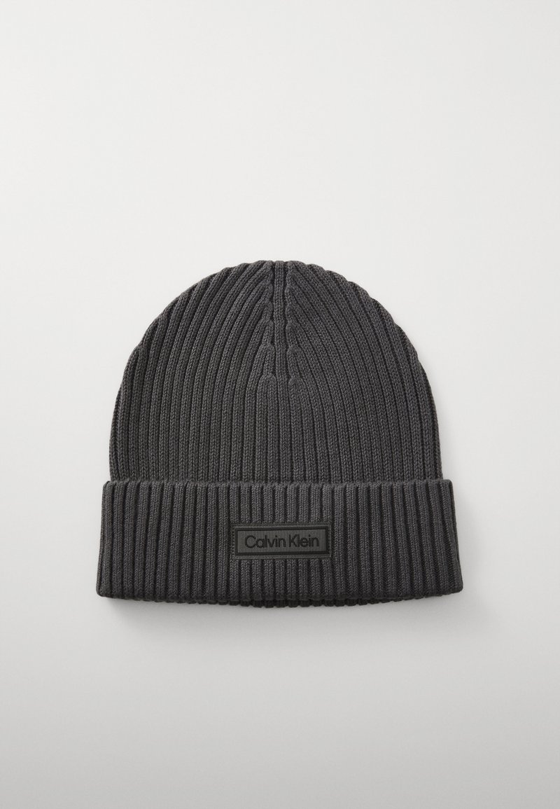 Beanie lavorato a maglia di colore grigio scuro. Presenta una texture a coste, un risvolto, e un'etichetta rettangolare nera con la scritta "Calvin Klein" in carattere bianco.