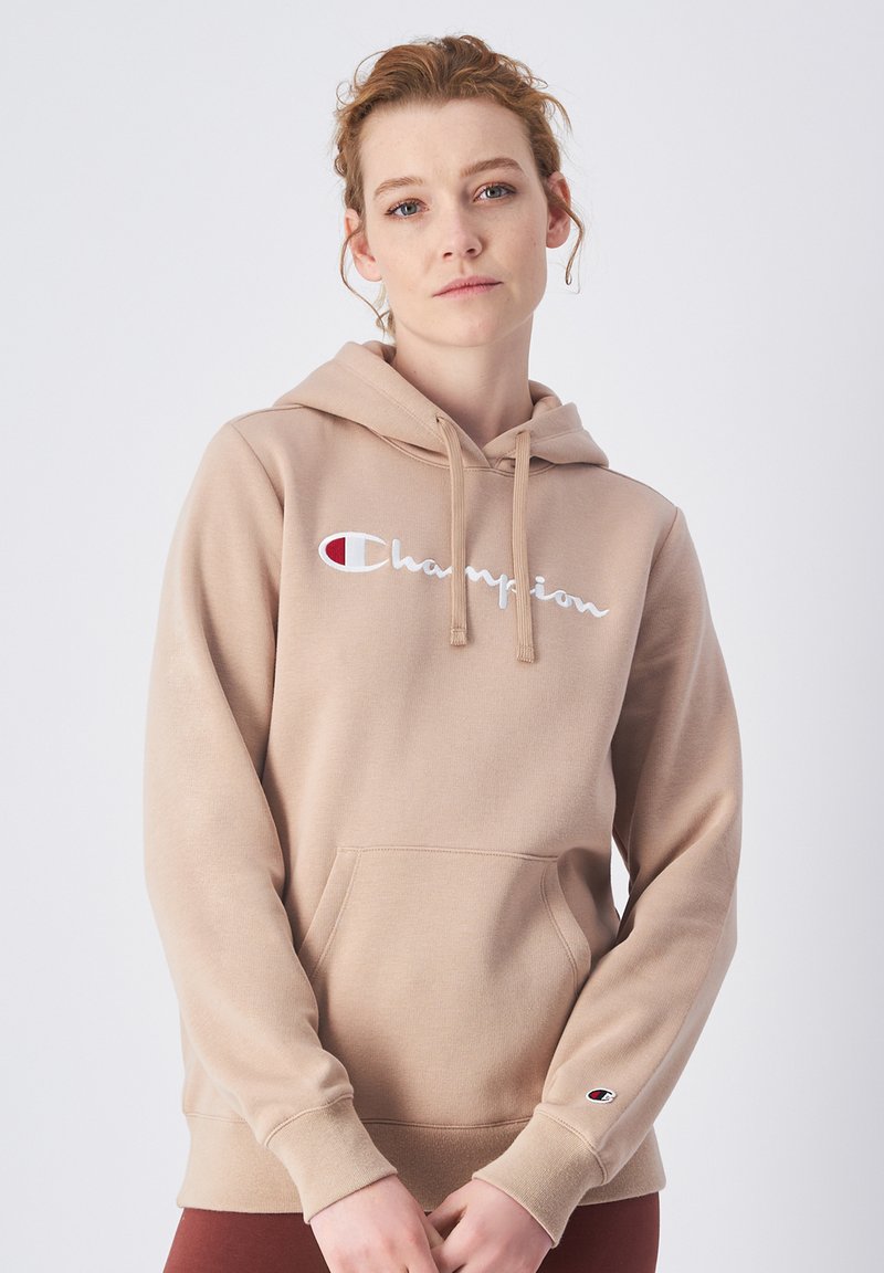 Sudadera beige hecha de un tejido suave, con un bolsillo frontal, capucha con cordón y el logo "Champion" en blanco con acentos rojos.