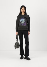 Felpa nera con design grafico di leopardo e testo "HEROIC", abbinata a jeans neri a zampa d'elefante e scarpe nere robuste. Borsa grigia.