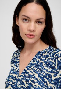 Blauw patroonblouse met V-hals en korte mouwen, met een crème en donkerblauw abstract patroon op een gestructureerde stof.
