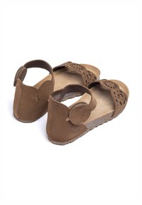 Braune Wildledersandalen mit durchbrochenem Blumendesign, verstellbarem Riemen auf der Rückseite und strukturierter Sohle, die eine schlichte und offene Form präsentieren.