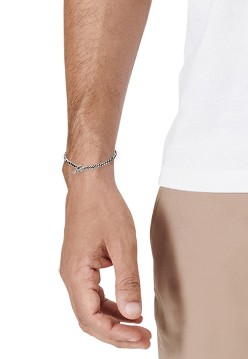 Hopeaketju ranteessa, jossa on toisiinsa kytkeytyviä lenkkejä ja klipsi, näkyvä tekstuuri, ja heijastaa valoa hienovaraisesti.