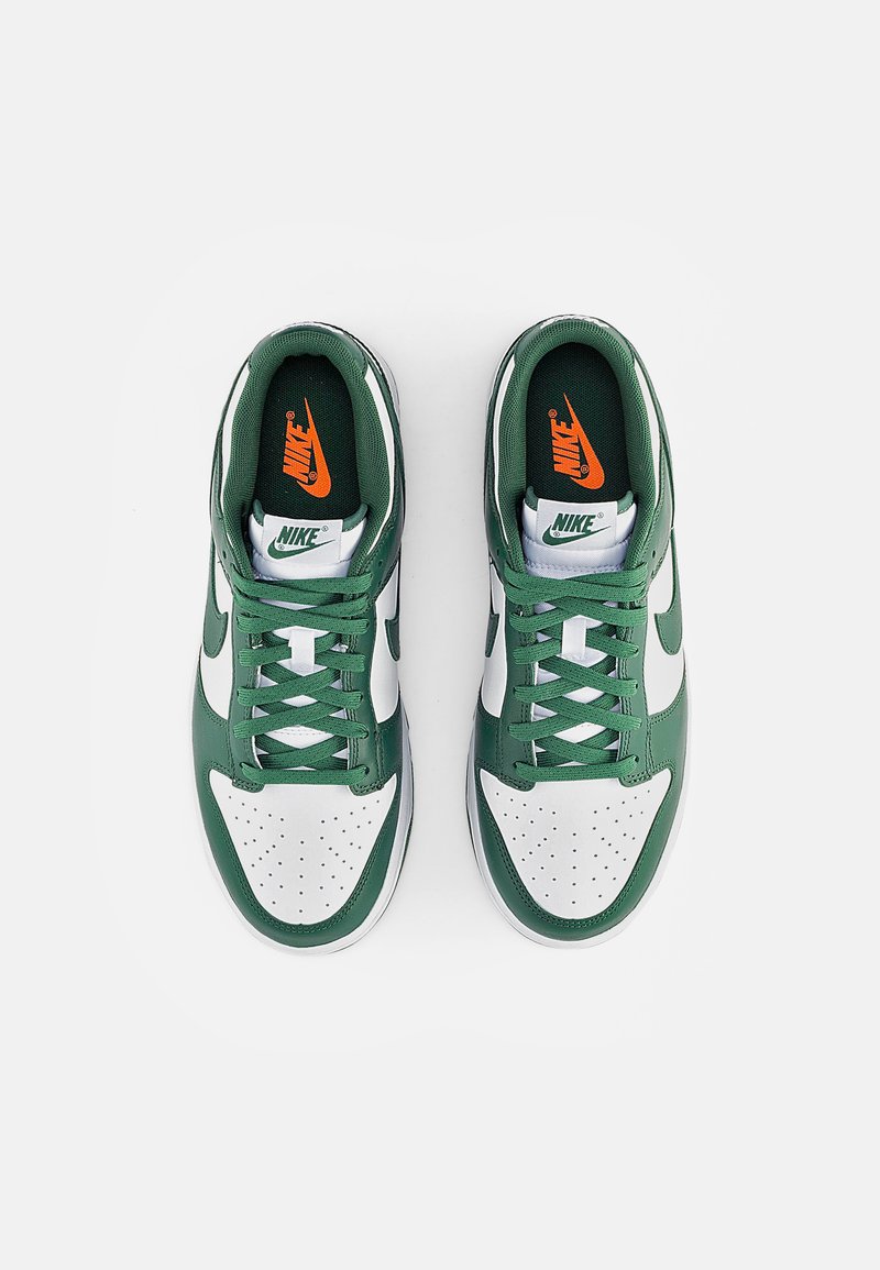 Zapatillas Nike con parte superior de cuero verde, caja de puntera sintética blanca, cordones verdes y logo naranja en la lengüeta verde oscuro. Detalle de puntera perforada.