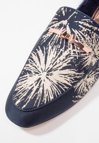 Chaussure plate marine avec motif feu d'artifice doré, bout arrondi et détail nœud en or rose sur une tige en tissu. Fini texturé sur le matériau.