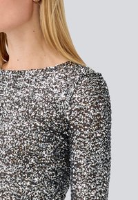 Silver sequined top with a rounded neckline and long sleeves. The texture is smooth and shiny, showcasing a dense pattern of sequins.