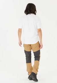 Beige en grijze outdoorbroeken hebben een taps toelopend ontwerp met versterkte knieën en ritsen bij de zakken. Gecombineerd met een witte shirt met korte mouwen.