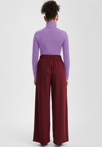 Fioletowa bluzka z długim rękawem i wysokim kołnierzem, zestawiona z wiśniowymi szerokimi spodniami o luźnym kroju, z elastycznym pasem i miękką fakturą.