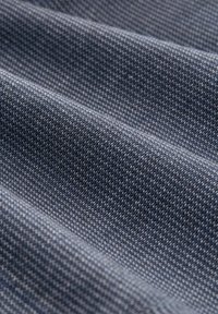 Denim stof in donkerblauw met een gestructureerd weefpatroon. Vert toont subtiele variaties in kleur en patroon van lichte naar donkere draden.