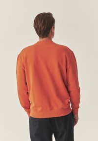 Orange bomuldssweatshirt med ribbet manchet og kant, afslappet pasform, rund halsudskæring og glat tekstur; set bagfra.