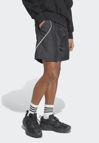 Sorte sportsbukser med hvid piping, der fremhæver et let design. Sammen med sorte sneakers og stribede hvide sokker.