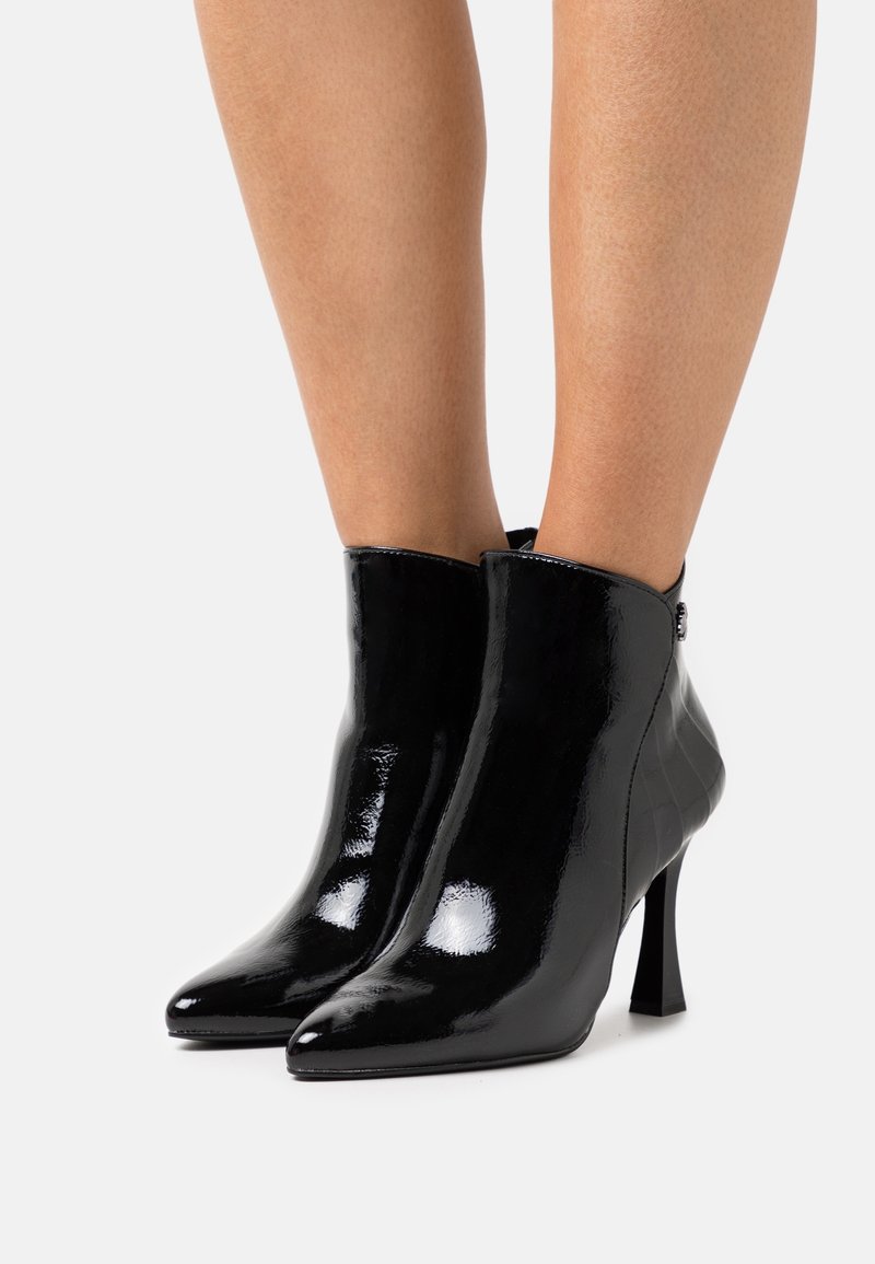 Bottines en cuir verni noir avec un bout pointu et un talon fin. Présente un côté texturé et une finition lisse et brillante. Fermeture à glissière à l'arrière.