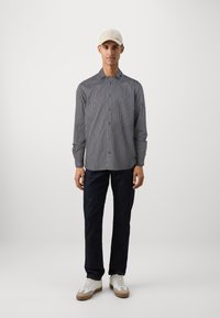 Stripet skjorte i marineblå og hvit, kombinert med mørk denim bukser og hvite sneakers, supplert med en lys beige caps.