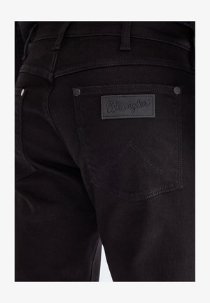 Nahaufnahme der Gesäßtasche einer schwarzen Denim-Jeans mit Wrangler Markenlabel und aufgenähtem „W“-Design.