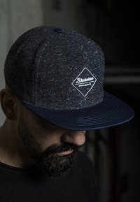 Dunkelblaue Snapback-Cap aus strukturiertem Stoff, mit einem weißen Diamant-Patch und dem "Blacksters"-Logo sowie einem flachen Schirm.